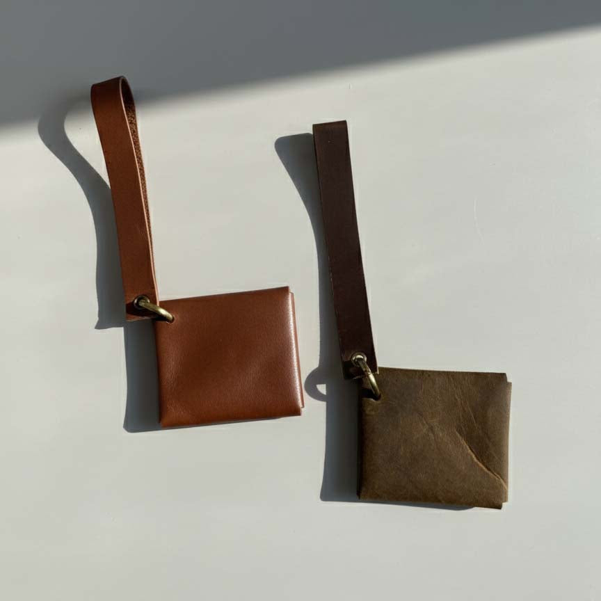 Two brown leather pouches with straps on a light gray background