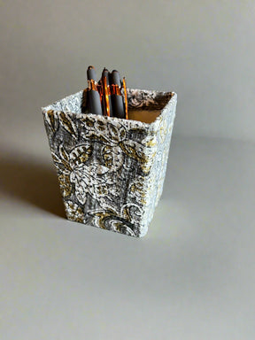 Decorative pen holder with patterned design containing pens on a plain background