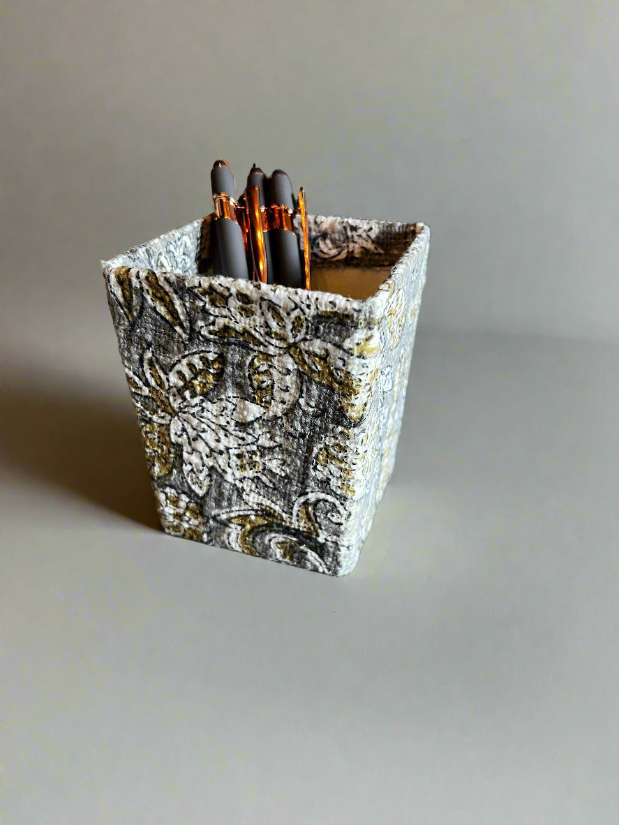 Decorative pen holder with patterned design containing pens on a plain background