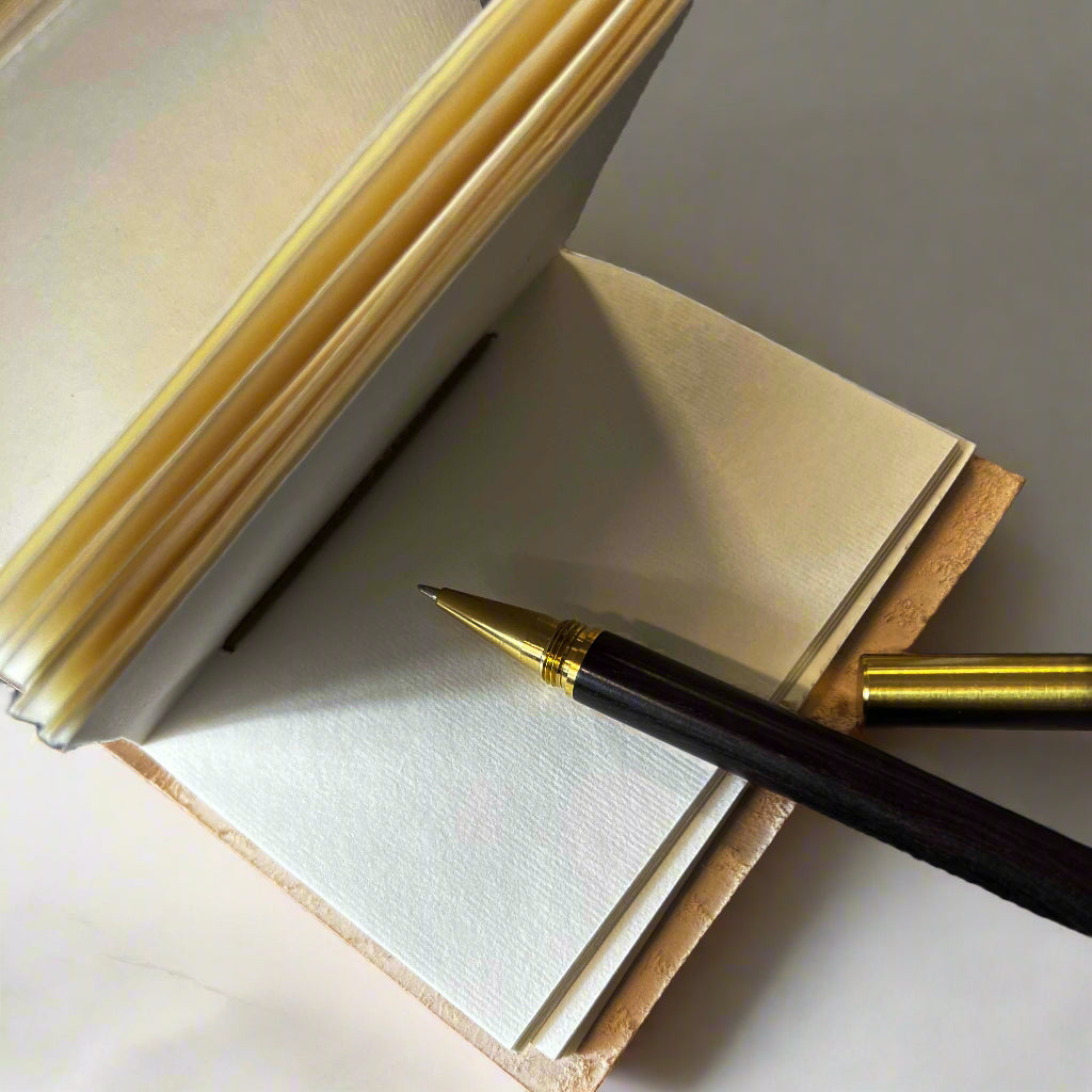 Fountain pen resting on an open leather notebook with unlined handmade paper pages.