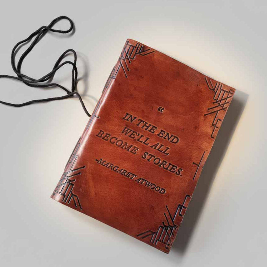 Close-up of embossed We All Become Stories quote on brown leather journal cover