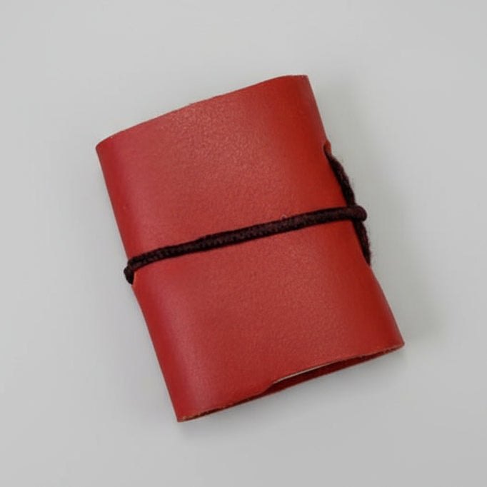 Red leather notebook with a black strap on a pink surface