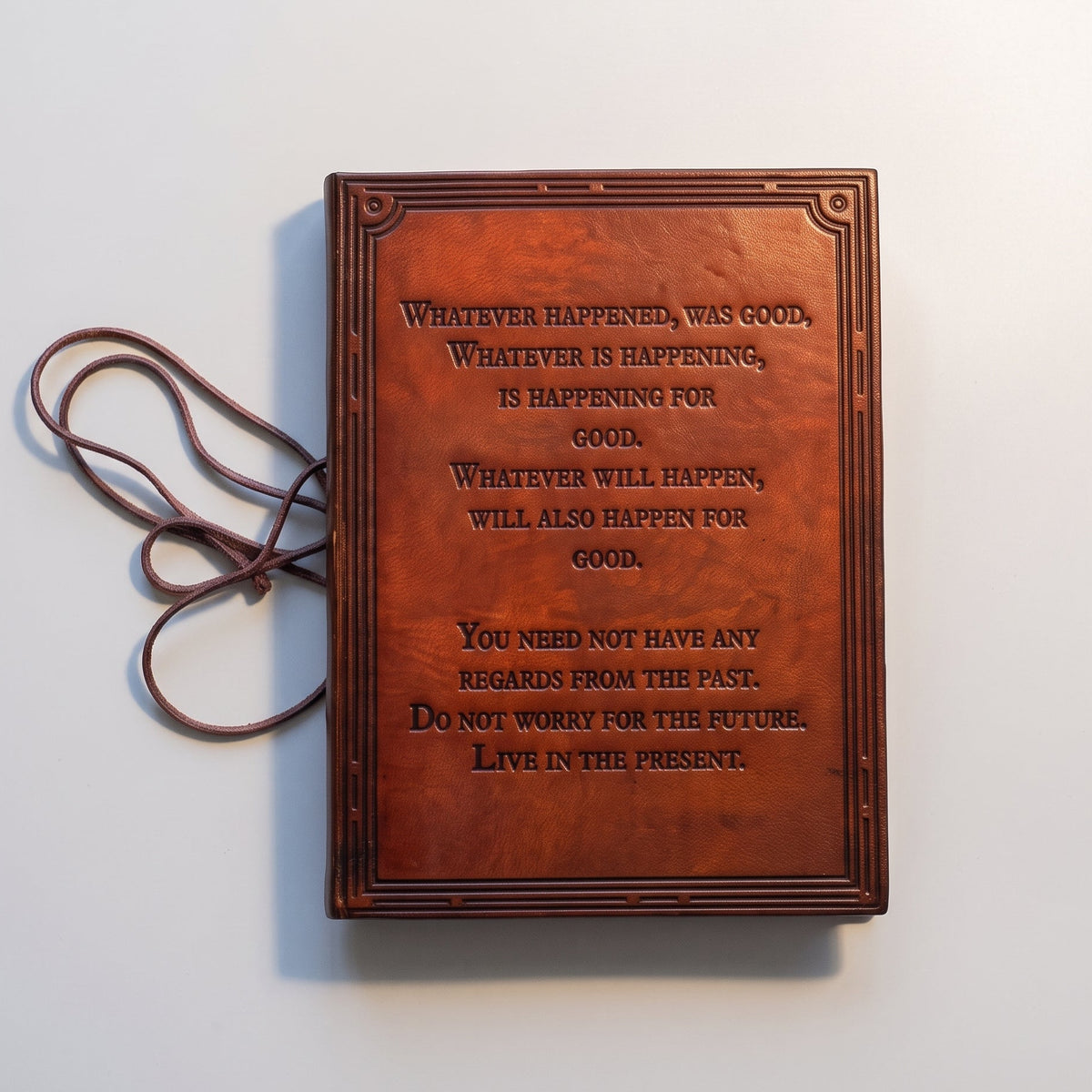 A brown leather-bound journal with embossed text on the front cover, photographed from above on a plain white background.