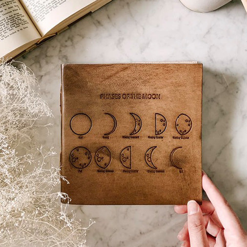 Moon Phases 7x7 leather journal with string-tie closure used as a bookmark